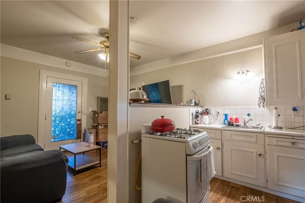 Kitchen and living area with white cabinets, a gas range, gray sofa, and blue-patterned glass door.