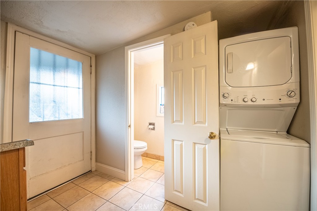 Laundry area with a stacked washer and dryer beside an open doorway to a bathroom.