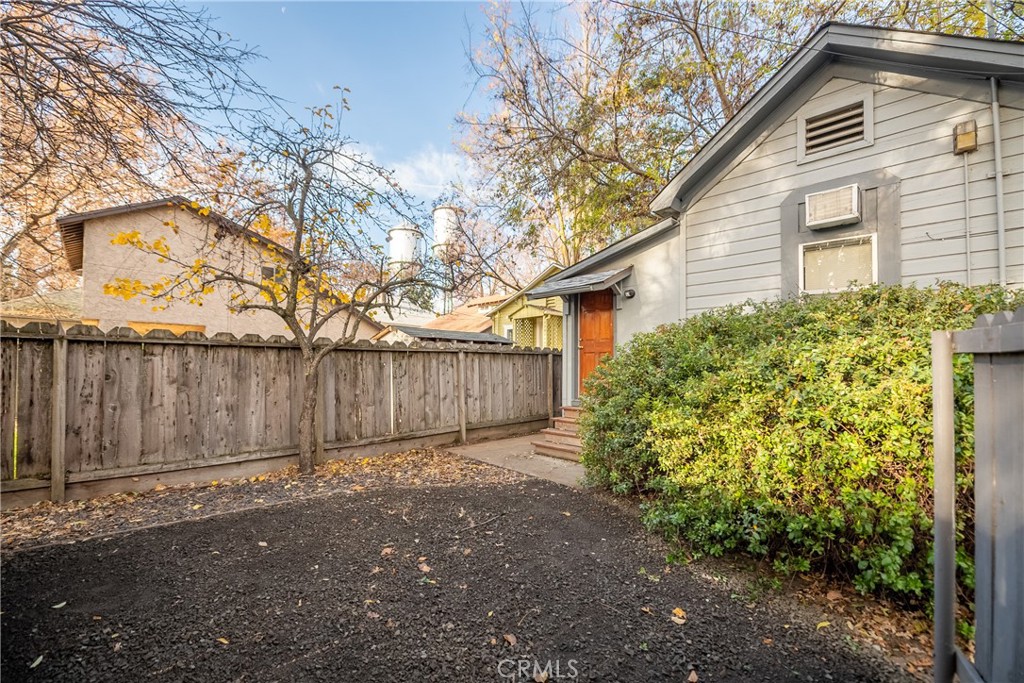 Gray-sided house with an orange door beside a gravel yard and wooden fence.