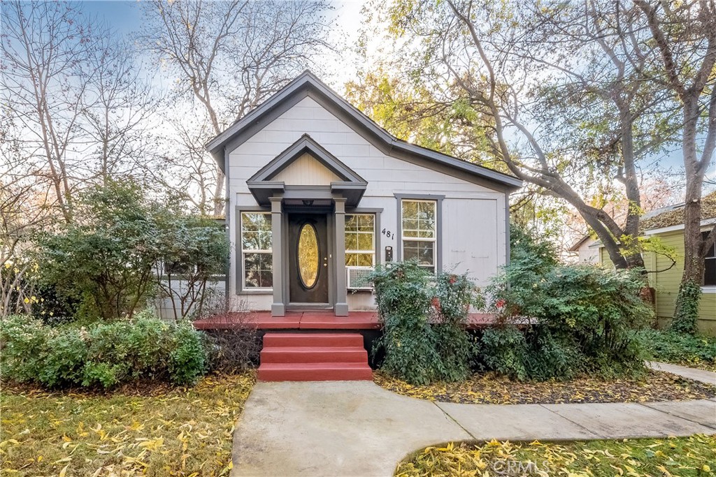 White gabled house with a dark oval-glass front door, red steps, and mature trees.