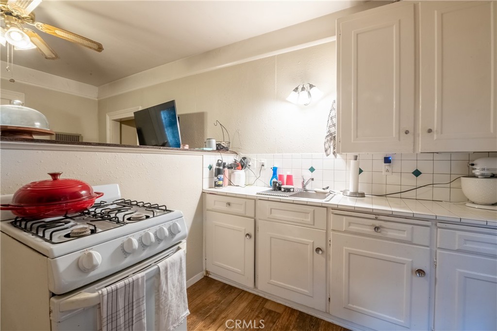 Kitchen with white cabinets, green-accented tile backsplash, and a gas range topped by a red Dutch oven.