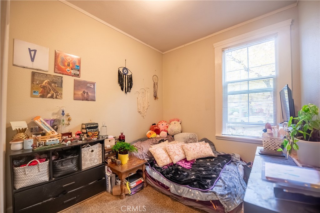 Bedroom with a dark patterned bedspread, pink pillows, and a large window with blinds.