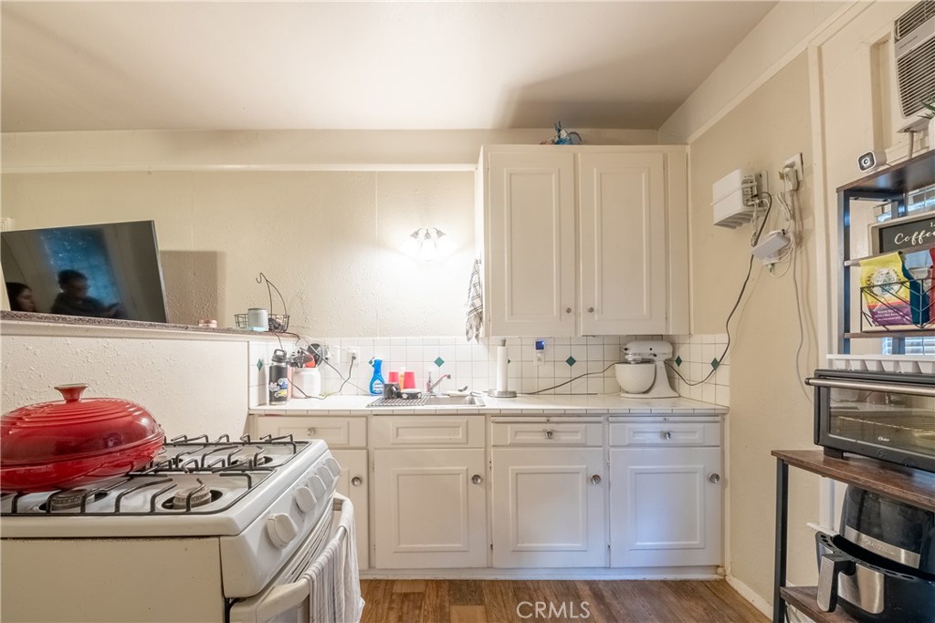 Compact kitchen with white cabinets, a gas range and red lidded pot, and wood-look flooring.