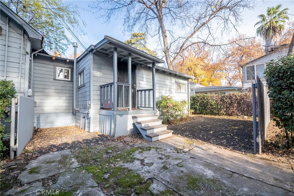 Gray house with a covered rear porch, steps, and fenced yard beside a cracked concrete patio.