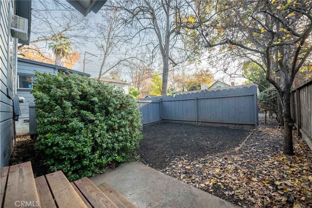 Fenced backyard with a concrete patio, wooden steps, a large shrub, and mature trees.