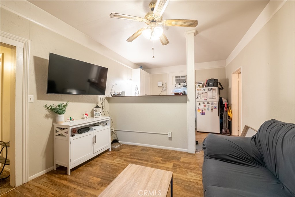 Living room with a gray sofa, wall-mounted TV, wood-look flooring, and an open kitchen behind a half wall.