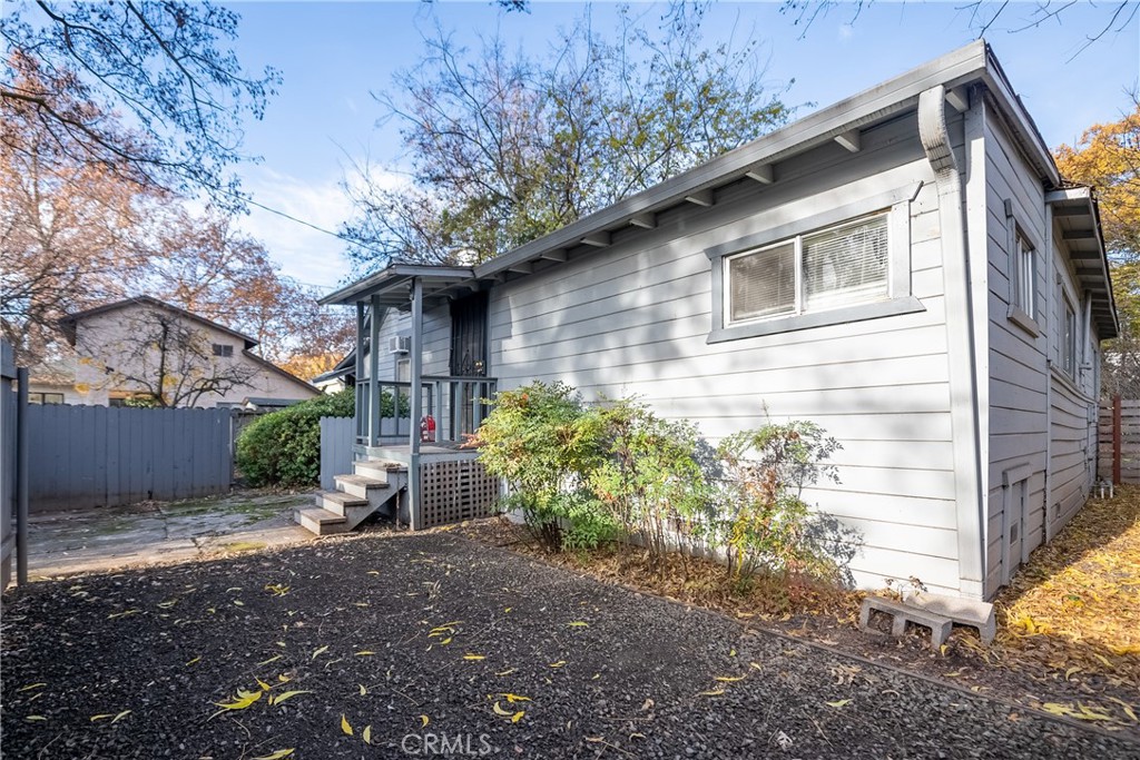 Light gray house with a covered side porch, shrubs, and a gravel yard.
