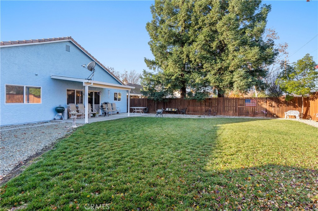 Fenced backyard with a broad lawn, mature trees, and a covered patio beside the house.