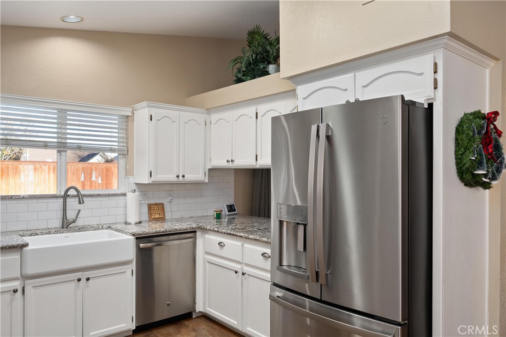 Kitchen with white cabinets, granite counters, farmhouse sink, and stainless steel appliances.