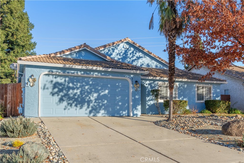Blue single-story home with a double garage, tiled roof, and rock landscaping.