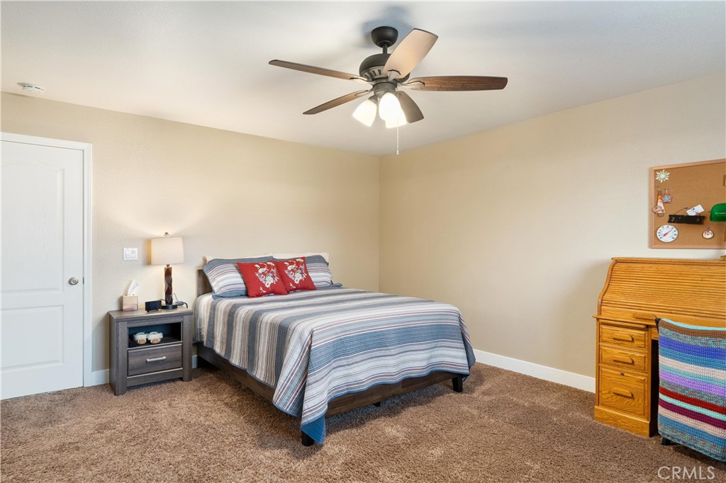 Furnished bedroom with striped bedding, red pillows, a wooden desk, and a ceiling fan.