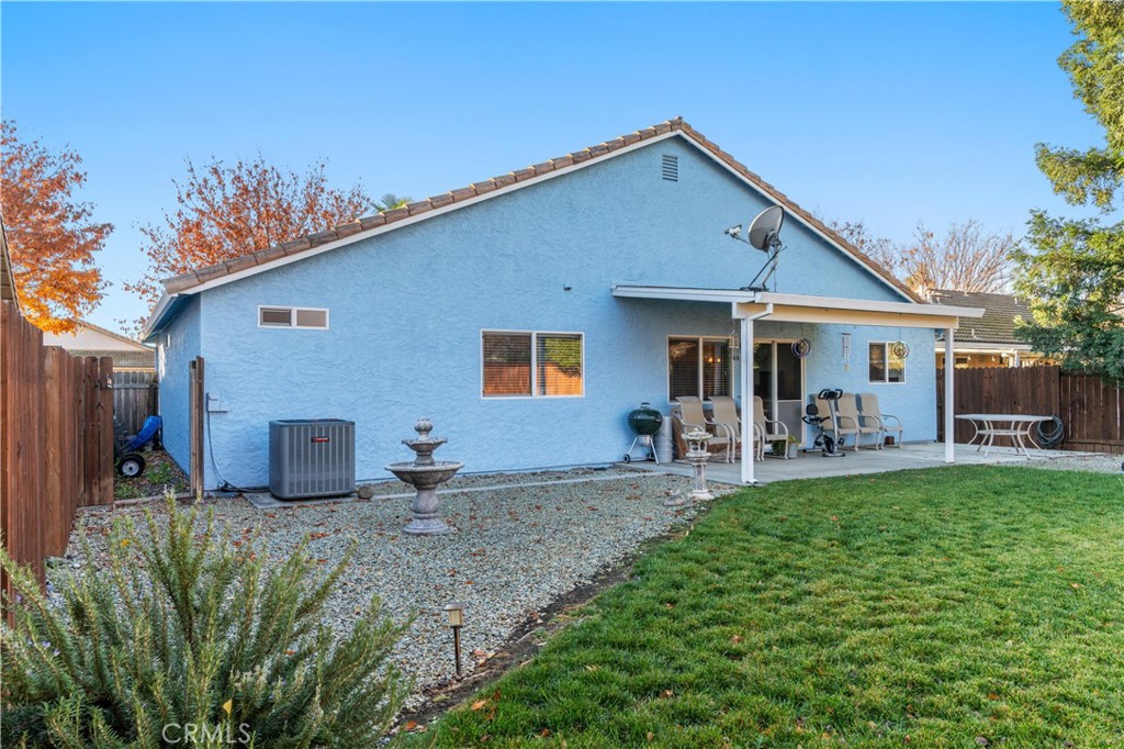 Blue stucco home's rear exterior with a covered patio, outdoor seating, and a green lawn.