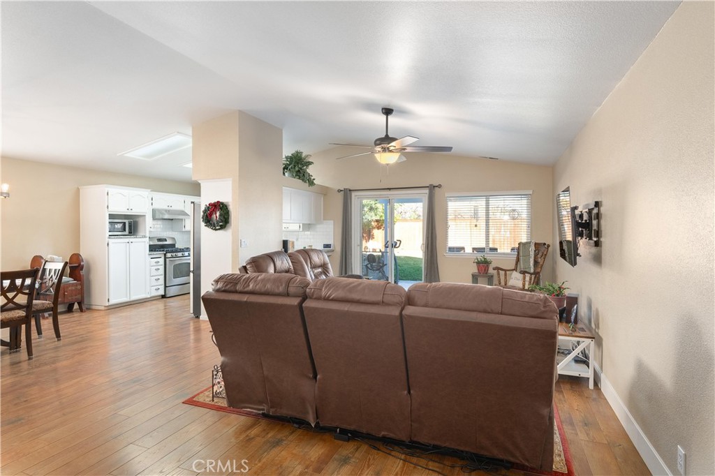Open-plan living room with a brown sectional, wood-look floors, and an adjoining white kitchen.