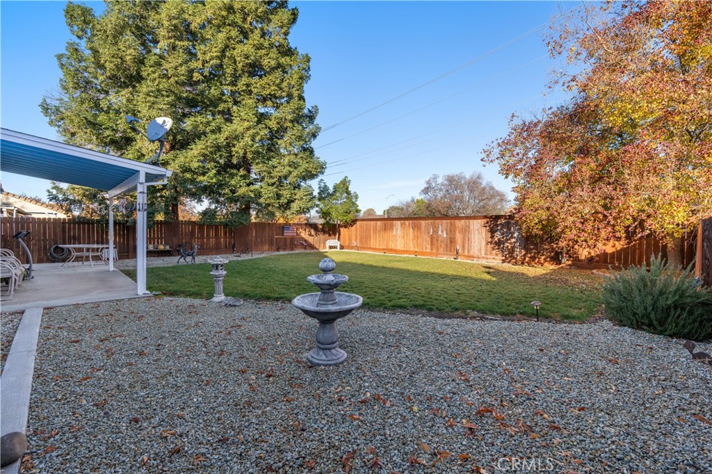 Fenced backyard with a tiered fountain, gravel patio, lawn, and covered seating area.