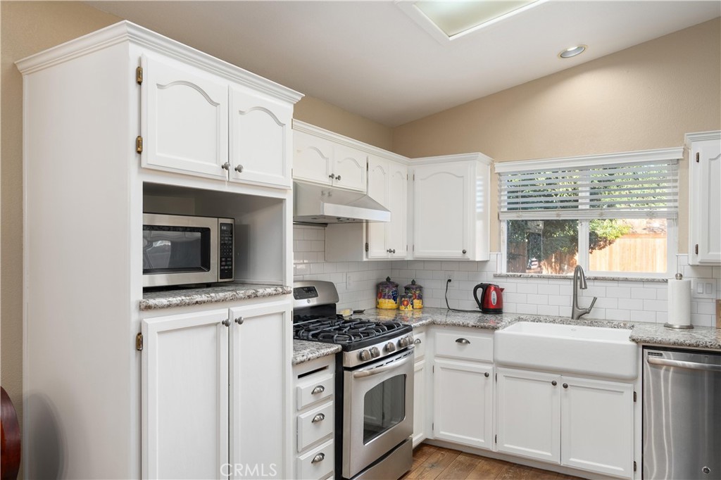 Kitchen with white cabinets, granite counters, farmhouse sink, and stainless steel appliances.