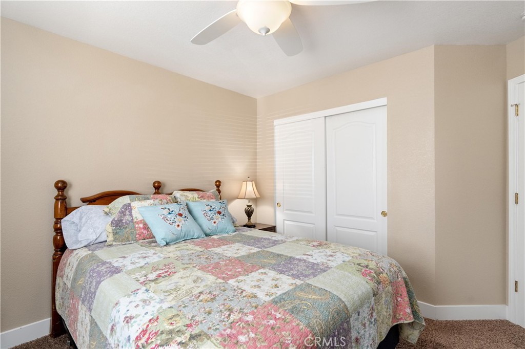 Bedroom with a colorful patchwork quilt, wooden bed, sliding closet doors, and ceiling fan.