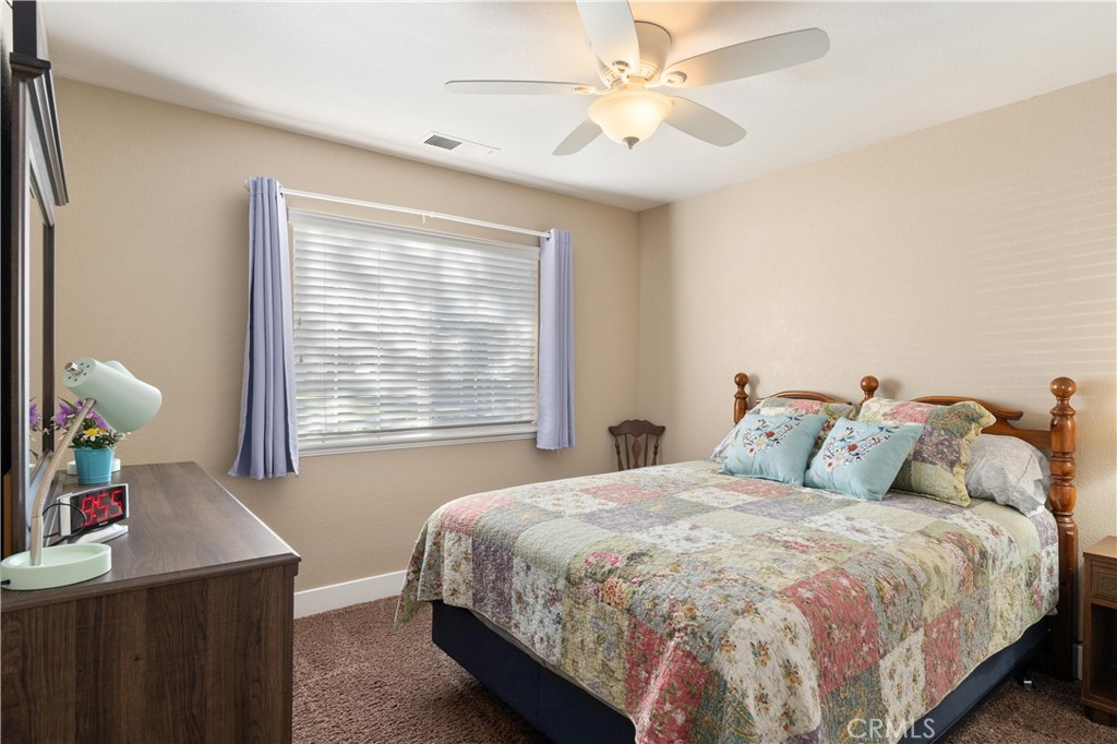 Bedroom with a patchwork quilt, lavender curtains, and a ceiling fan.