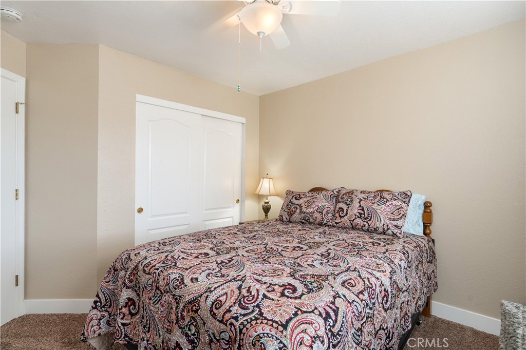 Bedroom with paisley bedding, a white closet, beige walls, and a ceiling fan.