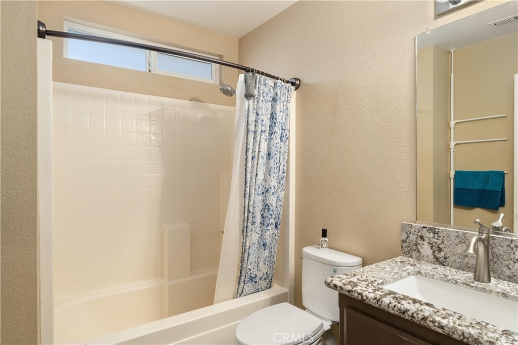 Bathroom with tiled tub and shower, patterned curtain, and granite vanity.