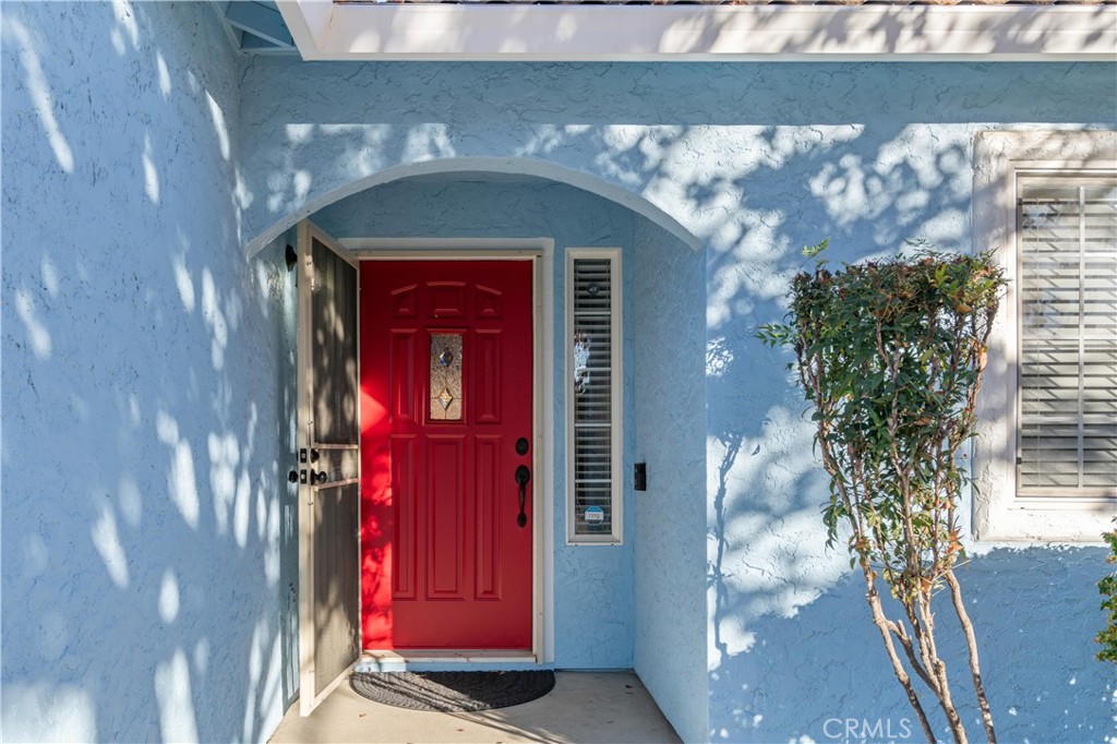Blue stucco entry with a bright red front door beneath an arched porch.
