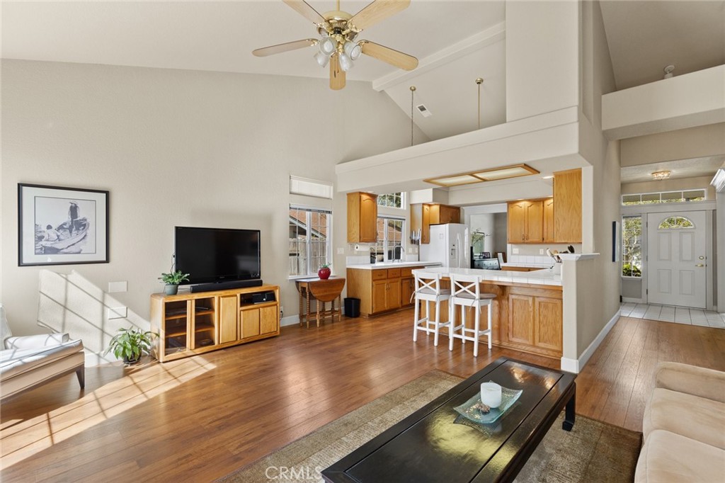Open-plan living room and kitchen with vaulted ceiling, hardwood floors, and a central island with bar stools.