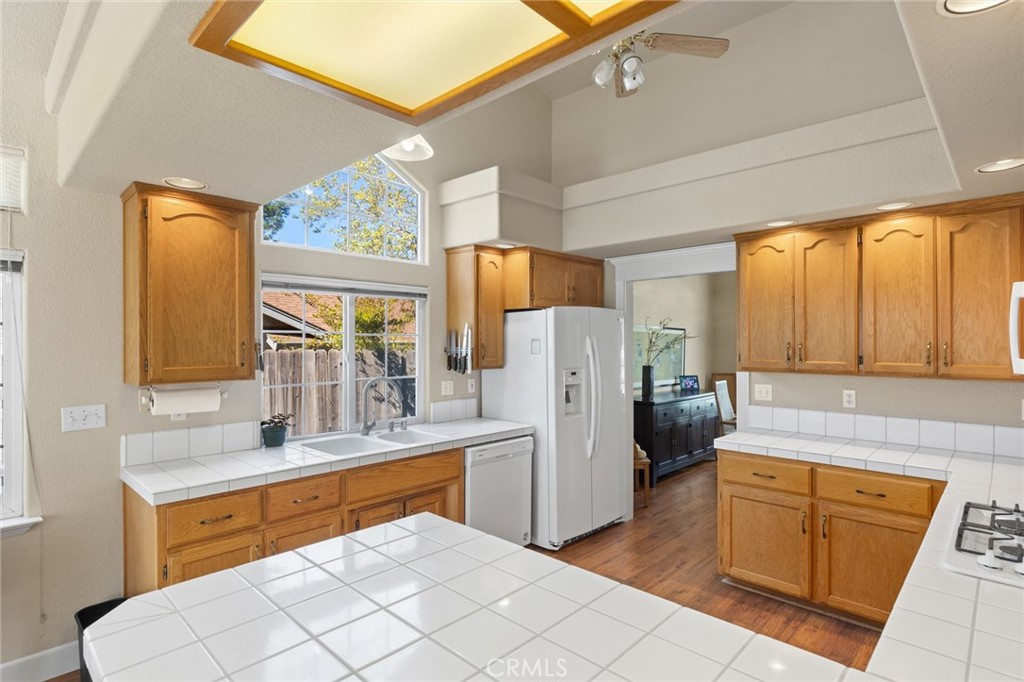 Kitchen with honey-colored cabinets, white tile counters, and tall windows above the sink.