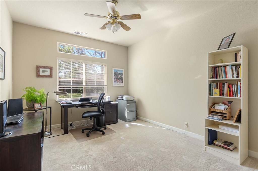 Furnished home office with a desk and computer beneath a wide window, plus a tall bookcase.