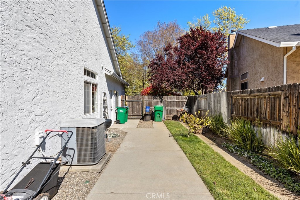 Side yard with a concrete walkway, wooden fence, lawn, and air-conditioning equipment beside a stucco home.