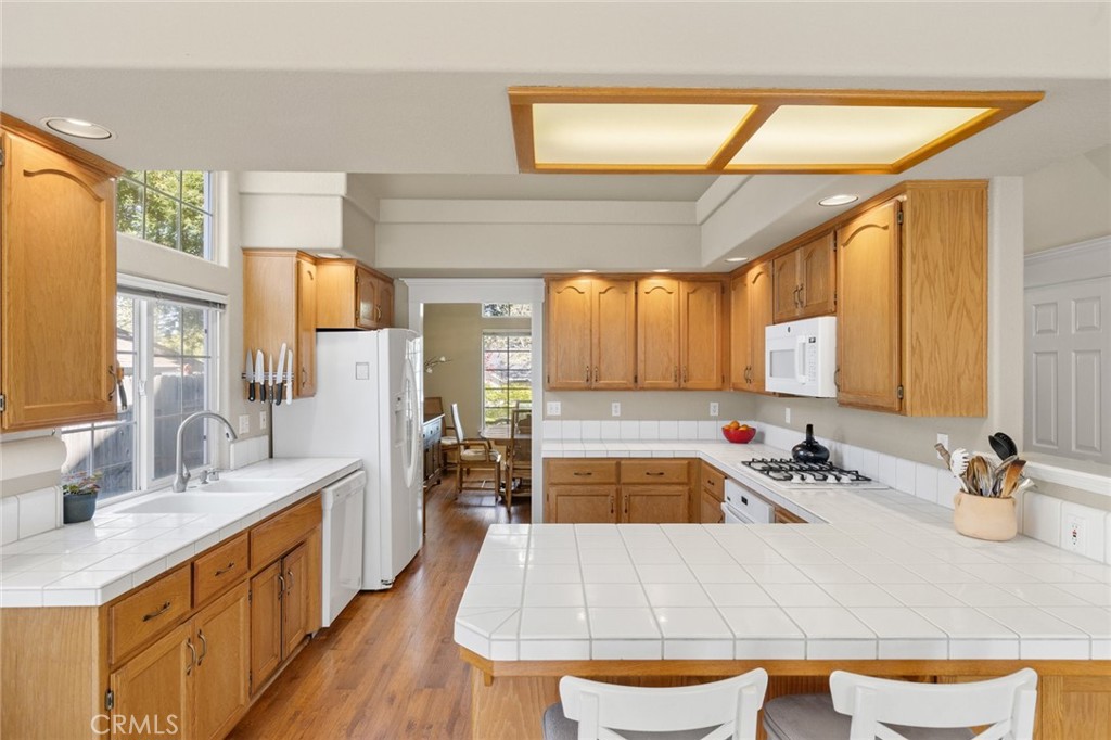 Kitchen with honey-colored wood cabinets, white tile counters, a large peninsula, and hardwood flooring.