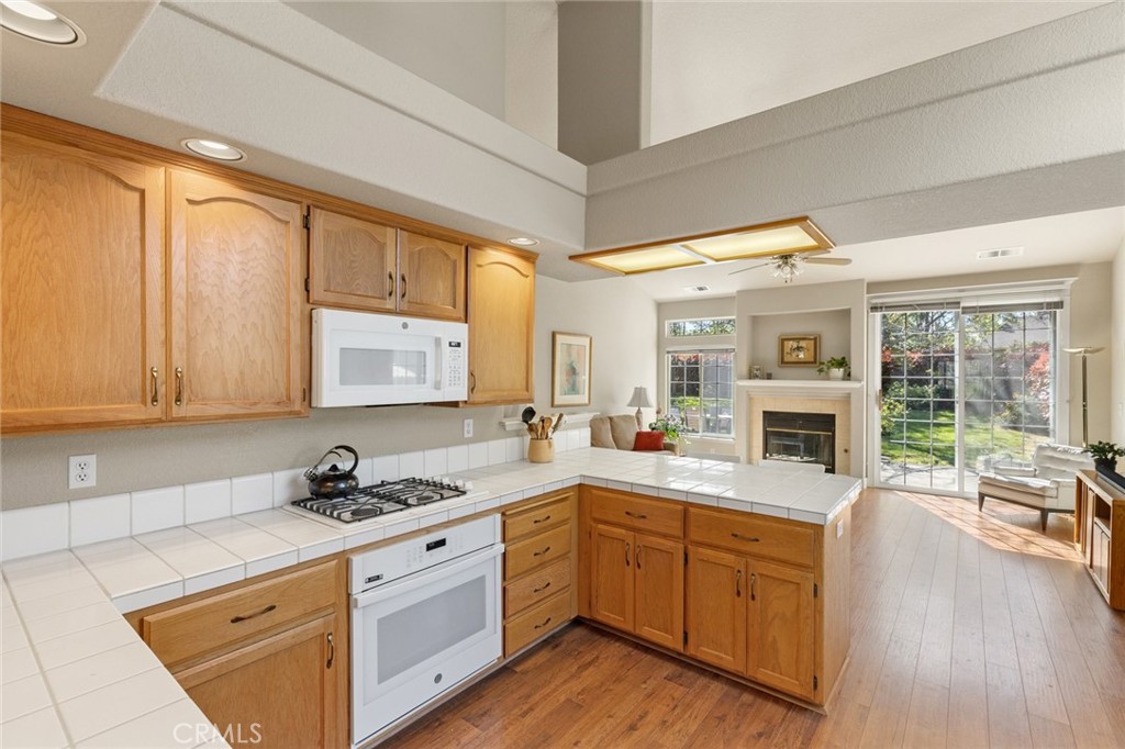 Kitchen with honey-colored cabinets and tiled counters opening to a living area with a fireplace and garden views.