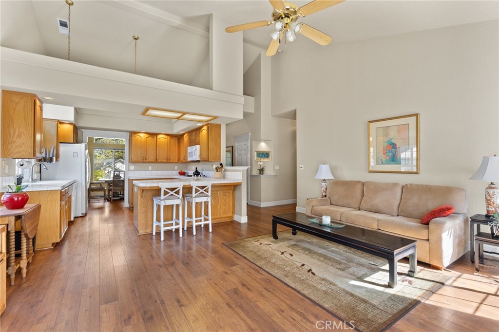 Open living room and kitchen with vaulted ceilings, wood floors, breakfast bar, and beige sofa.