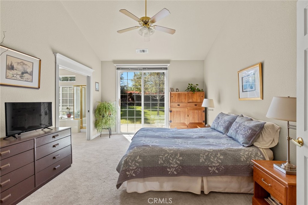 Bedroom with sliding glass doors overlooking a garden, a large bed, and a ceiling fan.