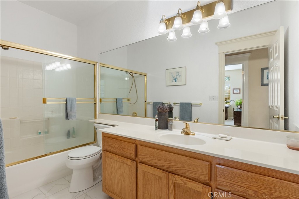 Bathroom with oak vanity, large mirror, and glass-enclosed tub with gold-tone trim.