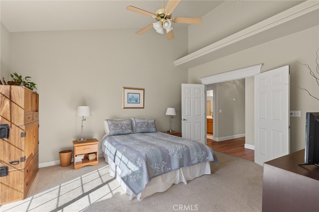 Furnished bedroom with a king bed, vaulted ceiling, ceiling fan, and open double doors.