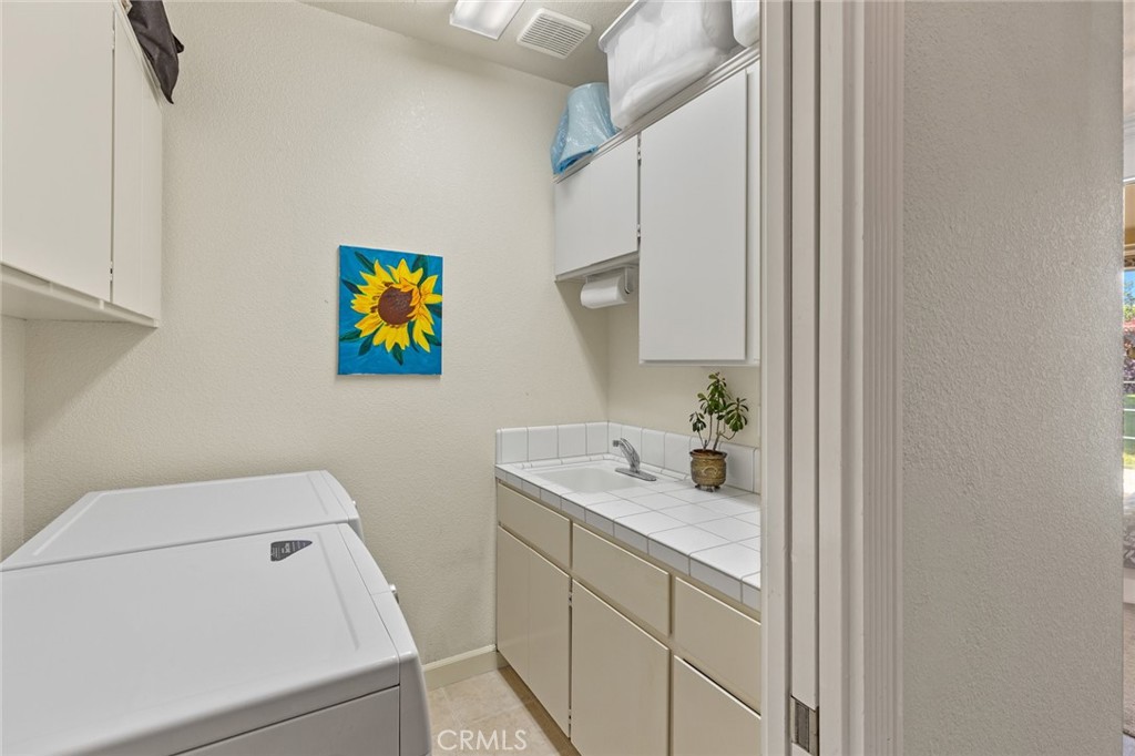 Laundry room with washer and dryer, built-in cabinets, tiled counter, utility sink, and sunflower artwork.
