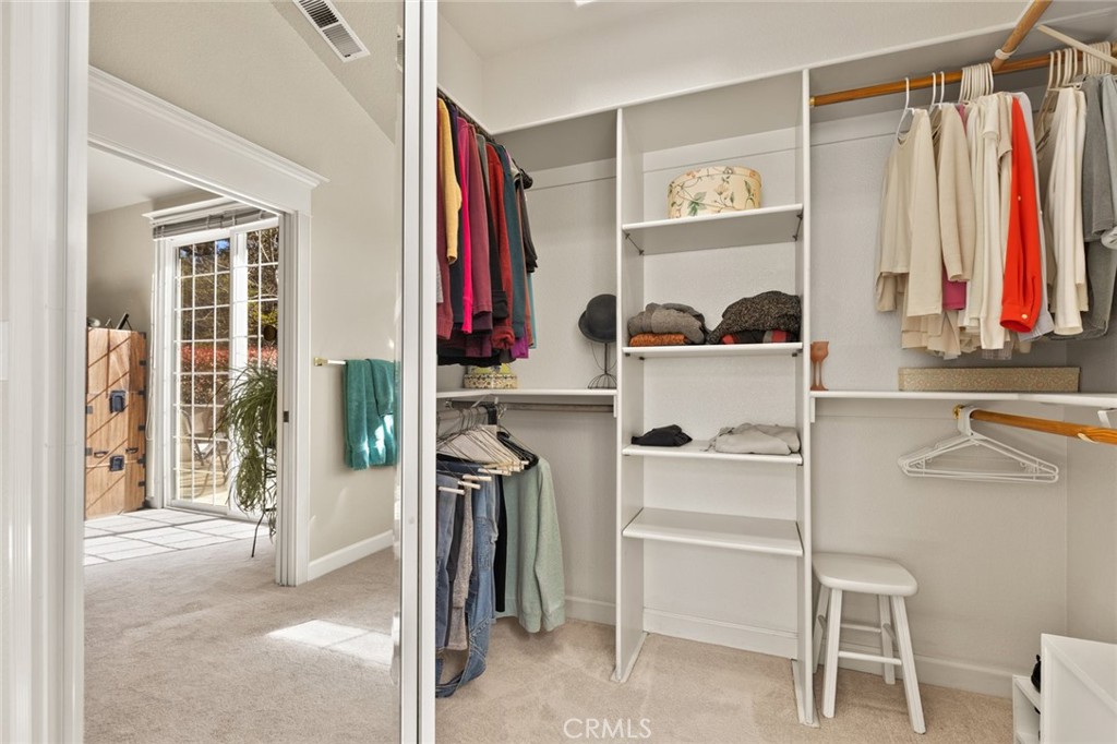 Walk-in closet with built-in shelving, hanging clothes, and a small stool.