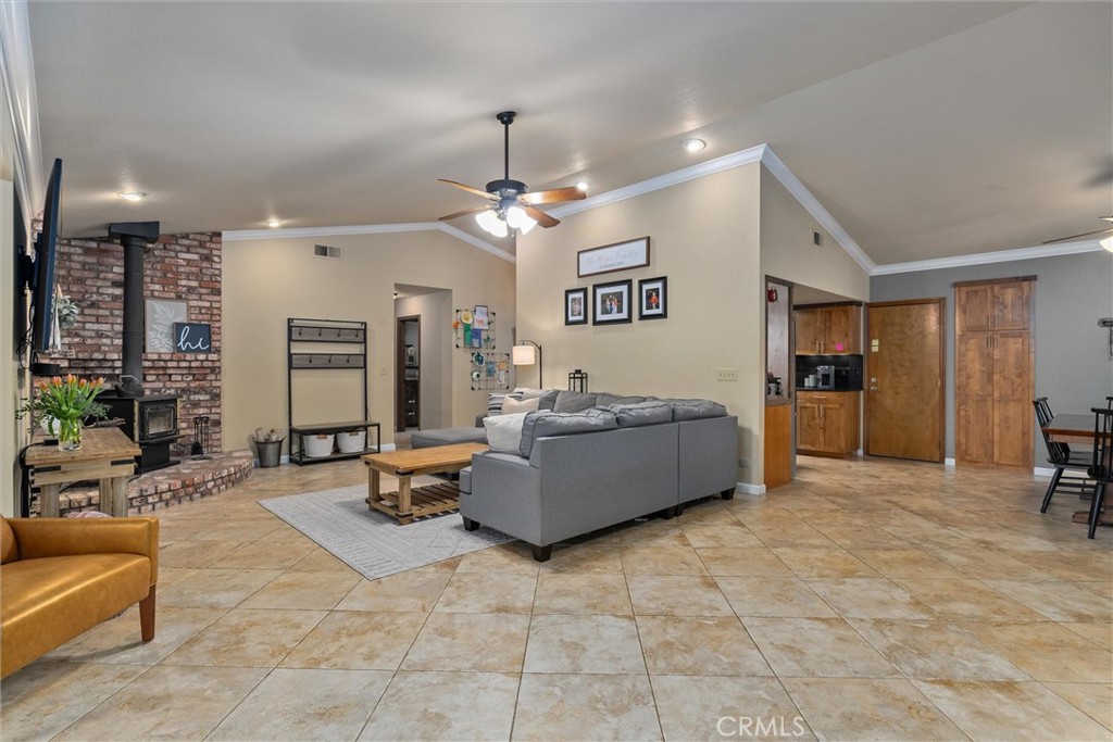 Living room with gray sectional, tiled floors, ceiling fan, and brick fireplace with wood stove.