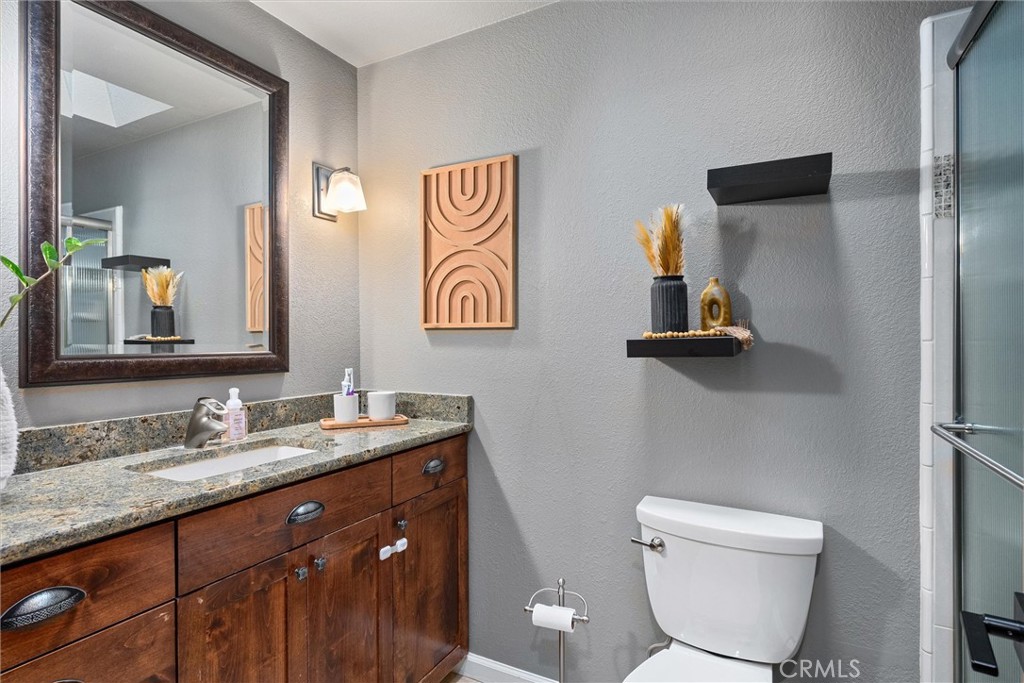 Bathroom with a dark wood vanity, speckled stone countertop, framed mirror, and glass shower.