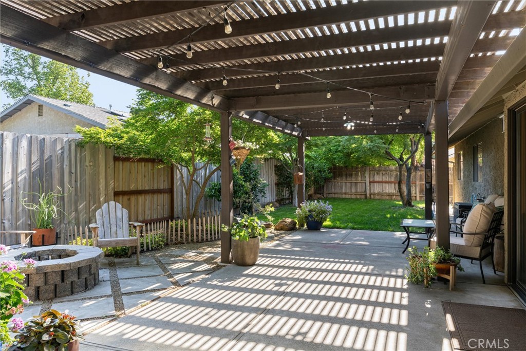 Backyard patio beneath a wooden pergola with string lights, outdoor seating, and a stone fire pit.