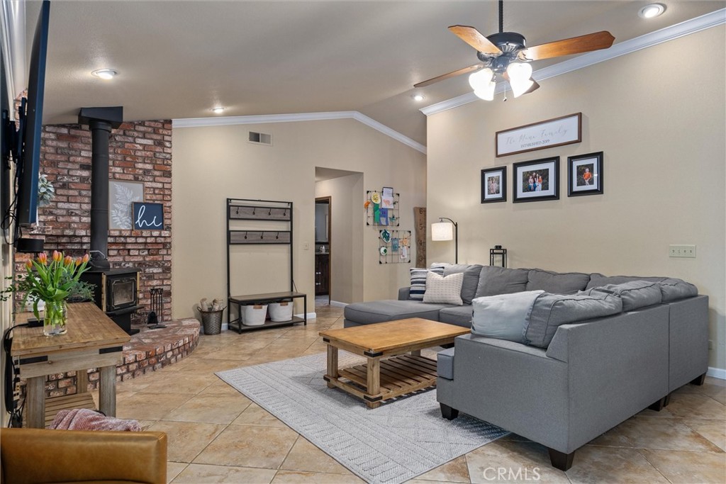 Living room with a gray sectional, tiled floors, and a brick fireplace with a wood stove.