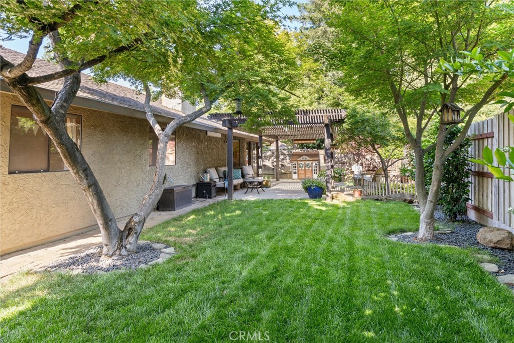 Shaded backyard with a green lawn, mature trees, and a covered patio with outdoor seating.