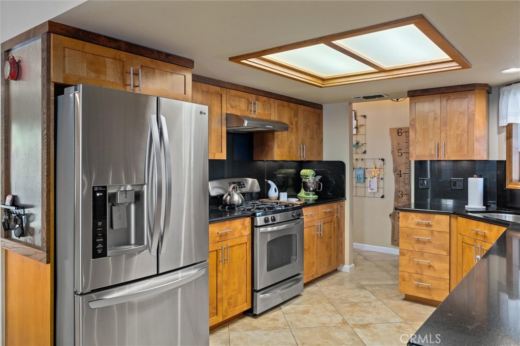 Kitchen with honey-colored cabinets, black countertops, and stainless steel appliances.