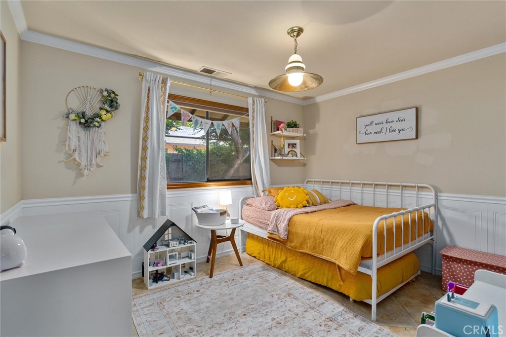 Bedroom with mustard-yellow bedding, a white metal bed, and a window with white curtains.