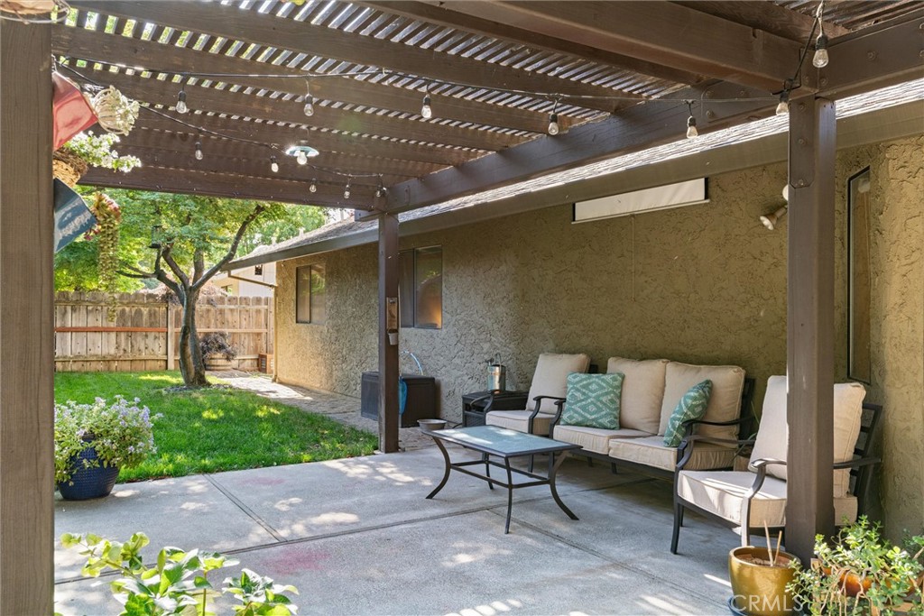 Backyard patio with a wooden pergola, cushioned seating, and a fenced lawn with a mature tree.