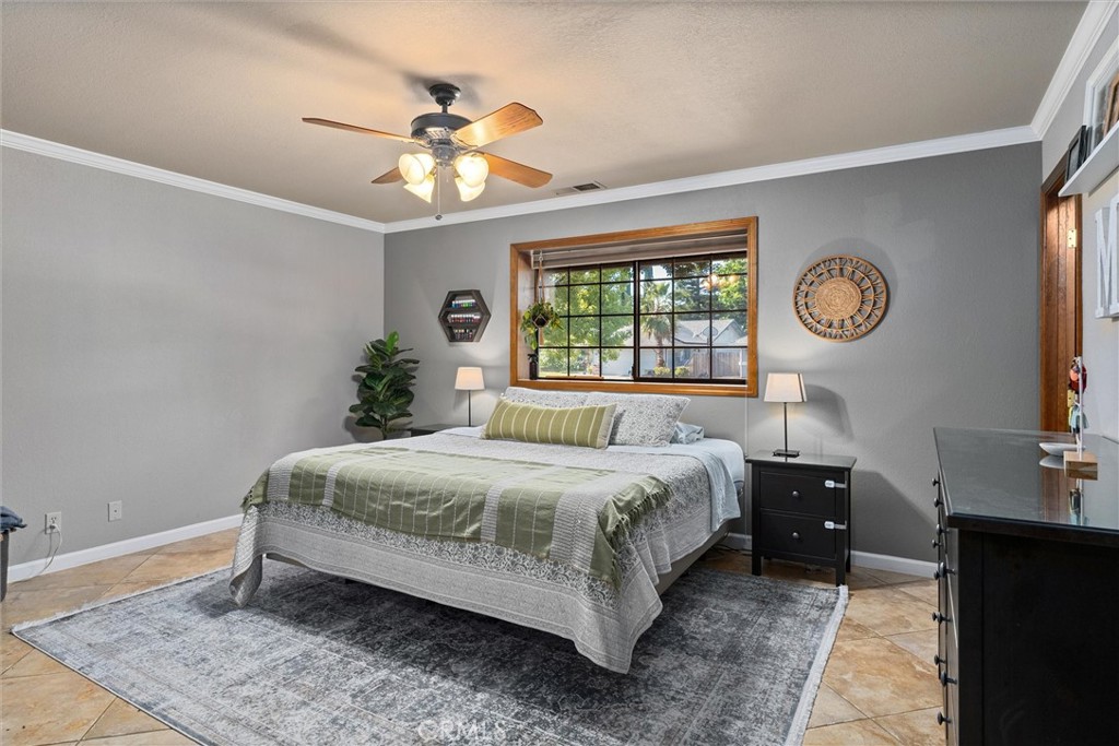 Staged bedroom with sage-green bedding, a wood-trimmed window, and a ceiling fan.