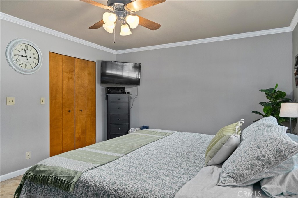 Bedroom with a large patterned bed, green throw, wooden closet doors, and wall-mounted television.