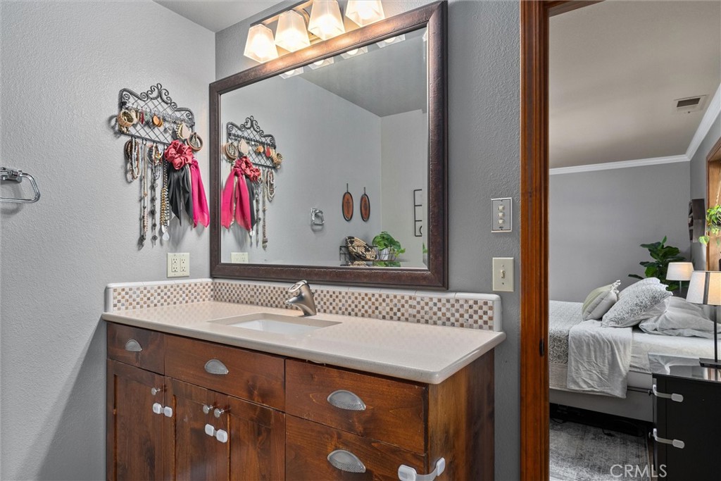 Bathroom vanity with a mosaic tile backsplash and framed mirror, looking through to a bedroom.