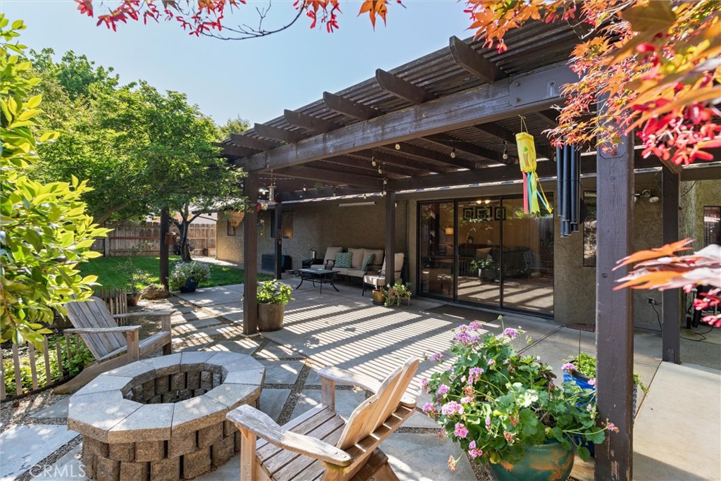 Backyard patio with a wooden pergola, outdoor seating, stone fire pit, and flowering planters.