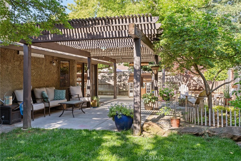 Backyard patio with a slatted pergola, outdoor seating, and leafy garden.