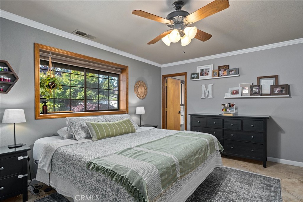 Bedroom with green and gray bedding, a large wood-trimmed window, and a ceiling fan.